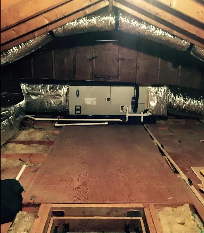 Attic crawlspace with insulated HVAC unit centered on exposed wooden rafters and floor joists.