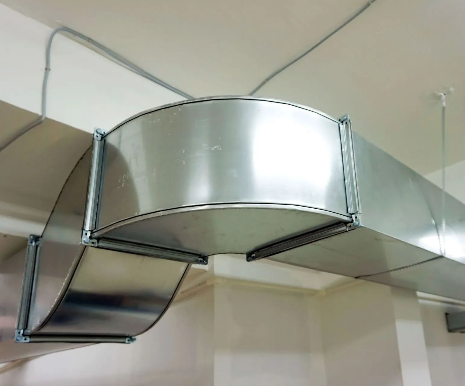 Metal HVAC ductwork near the ceiling in an indoor room with exposed pipes and vents