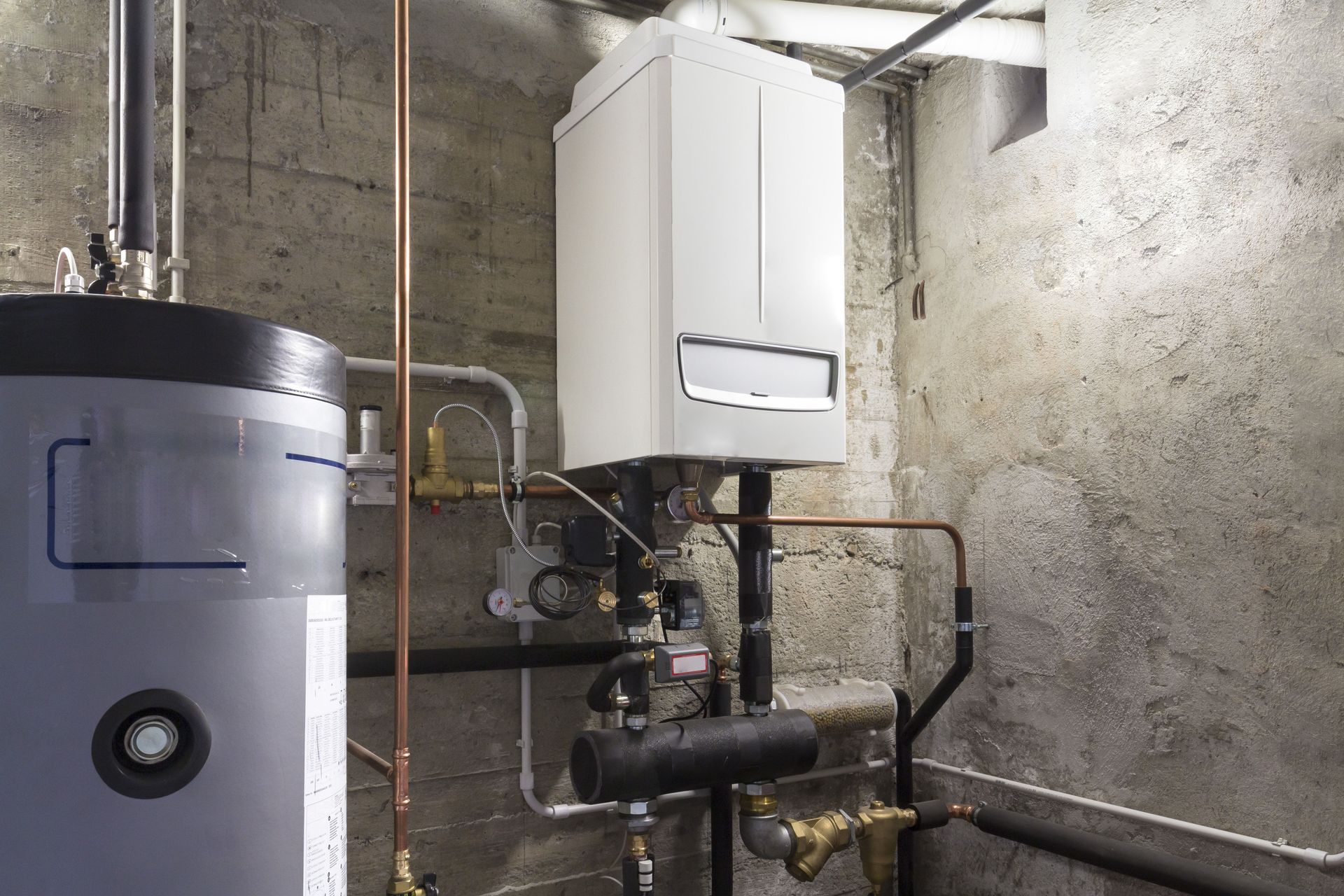Boiler room with a water heater, wall-mounted boiler, and exposed pipes against concrete walls