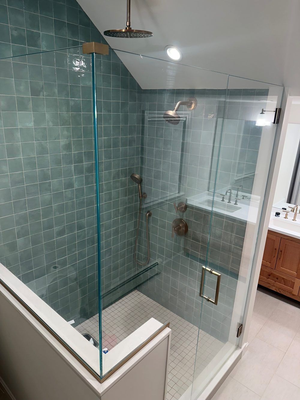 Modern bathroom shower with teal tile, glass enclosure, and gold fixtures.