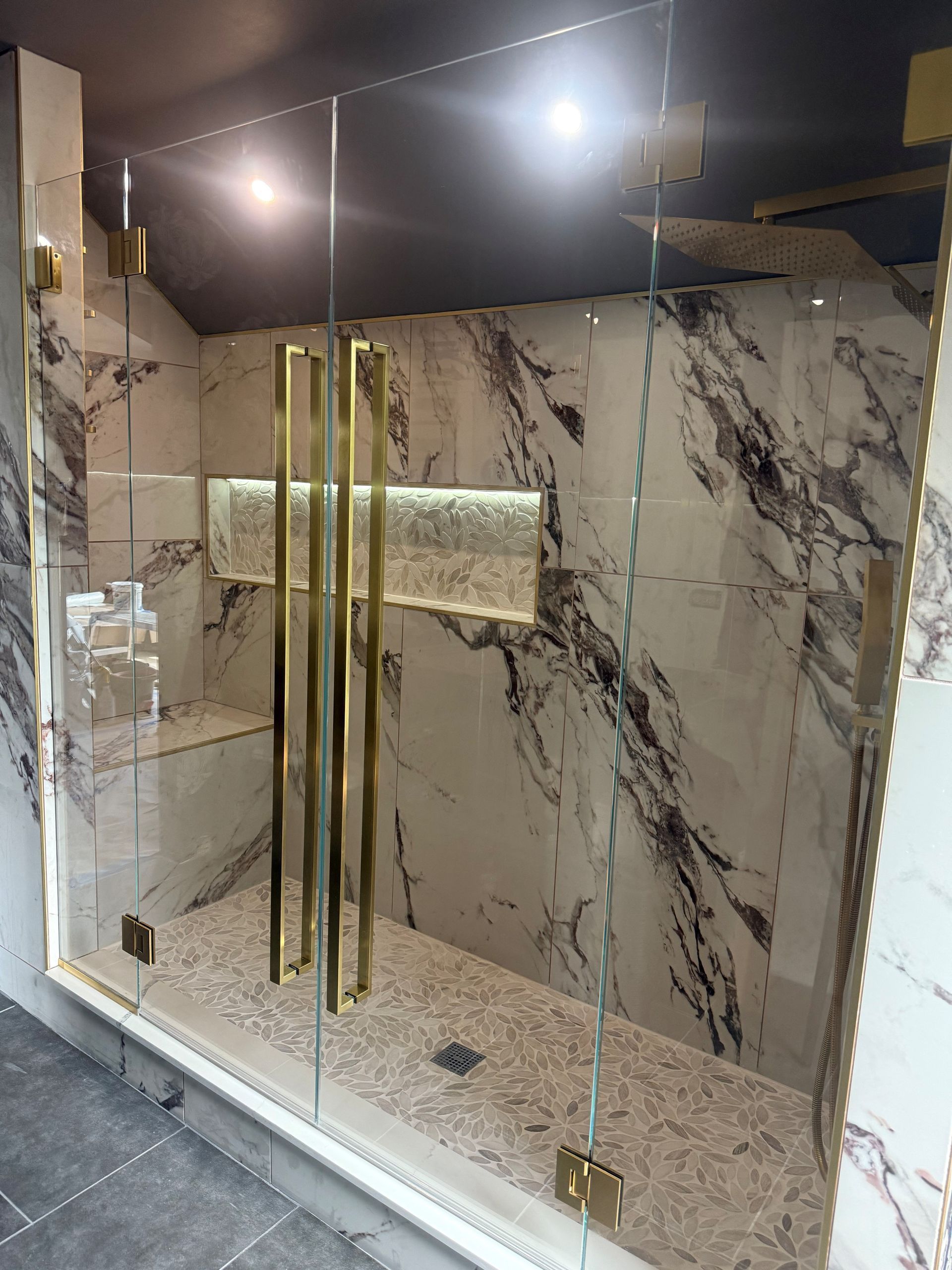 Elegant marble shower with gold hardware, frameless glass door, and a pebble floor.