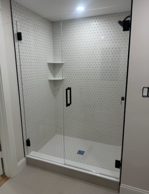 Glass shower with white tile walls and floor, black fixtures and handle, and two built-in shelves.
