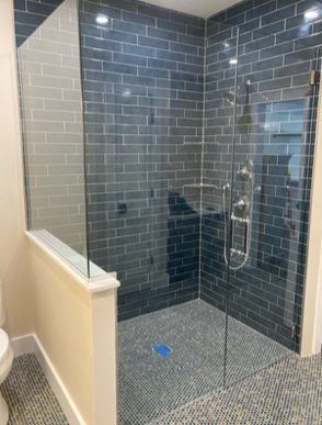 Shower with blue brick-like tile walls and small mosaic floor, glass enclosure, and silver fixtures.