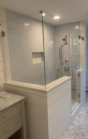 Modern white tiled shower with glass doors and a marble-topped vanity.