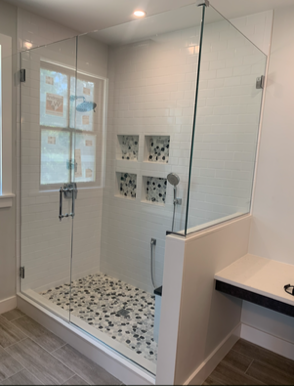 Modern walk-in shower with glass doors and pebble floor. White tile walls with built-in storage.