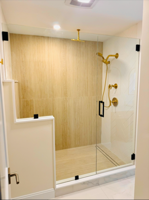 Modern bathroom with glass shower enclosure, gold fixtures, beige tile walls.
