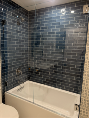 Bathroom with blue brick tiles, white tub, and glass shower door.