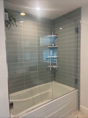 Bathroom with a glass shower door and blue-gray tiled walls. A white tub is visible below the glass.