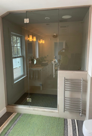 Glass shower enclosure in a bathroom, with a window and towel warmer. Green rug.
