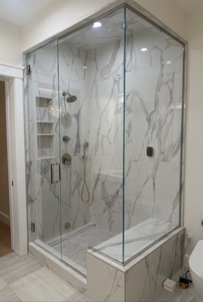 Modern shower with glass walls, marble-patterned walls and floor, built-in shelving and bench.