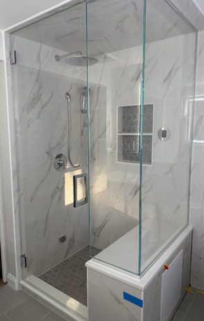 Glass shower enclosure with marble tile walls, bench seat, and rain shower head.
