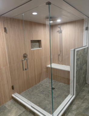 Modern shower with clear glass enclosure and beige and gray tiling. Features a built-in bench and recessed shelf.