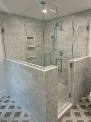 Modern shower with glass walls, marble tile, and a built-in shelf.