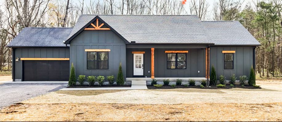 A gray house with a black garage door is sitting on top of a dirt field.