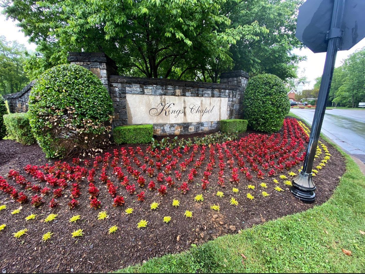 A sign for kings ridge is surrounded by flowers and bushes.