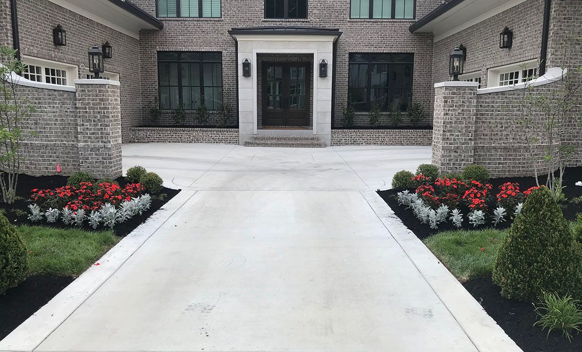 A large brick house with a concrete driveway and flowers in front of it.