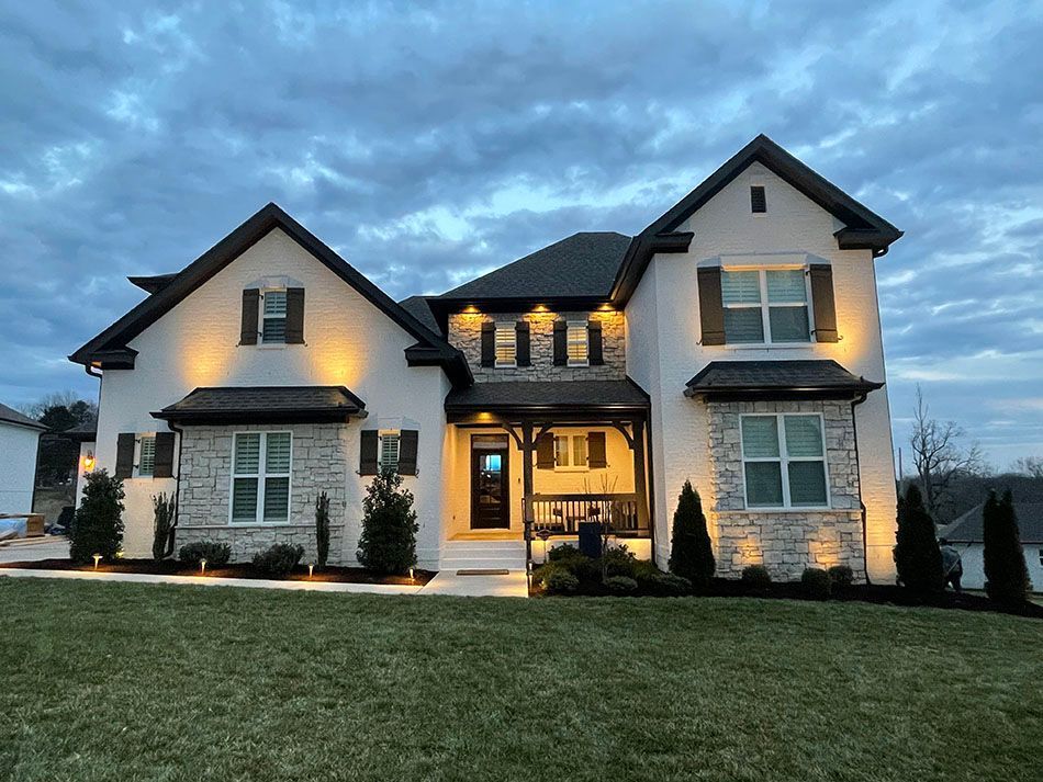 A large white house with black shutters is lit up at night.