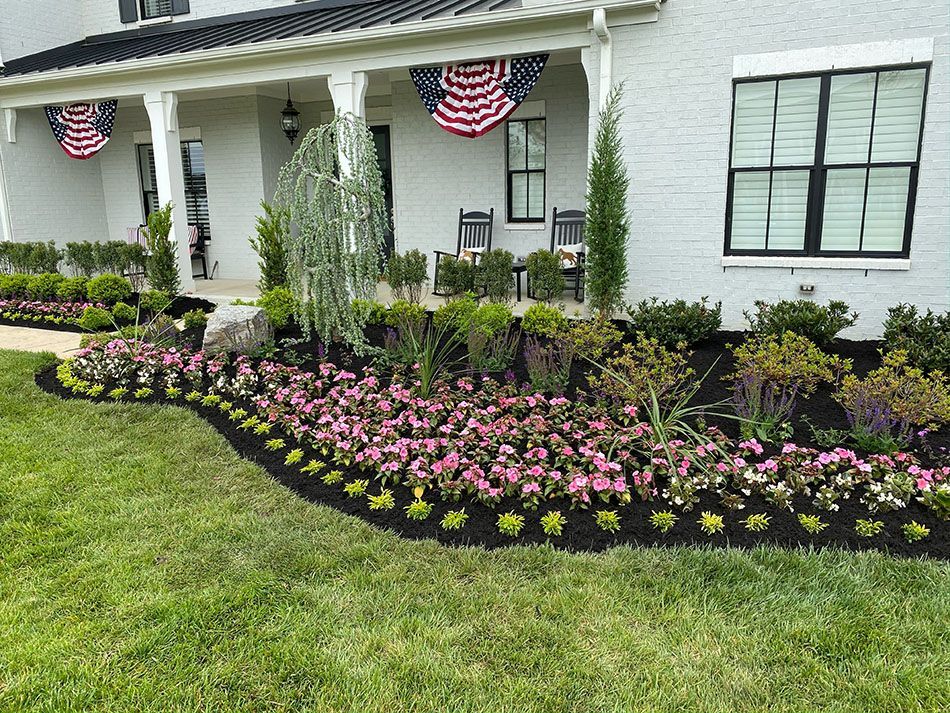 A white house with a lush green lawn and flowers in front of it.