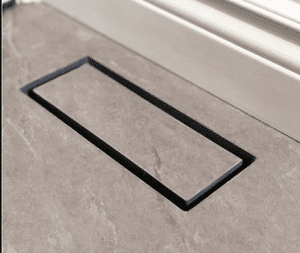 Black-framed rectangular floor hatch in a concrete floor near a wall