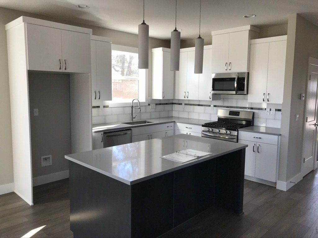 Bright modern kitchen with white cabinets, gray tile, and a dark island