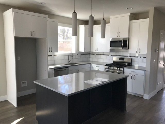 Modern kitchen with white cabinets, gray countertops, and a dark island under pendant lights