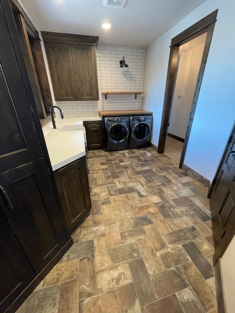 Narrow laundry room with washer and dryer, sink, shelves, and wood-look tile floor.