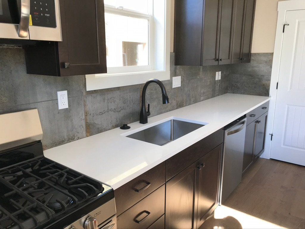 Modern kitchen with dark cabinets, white countertops, black faucet, gas stove, and stainless dishwasher.