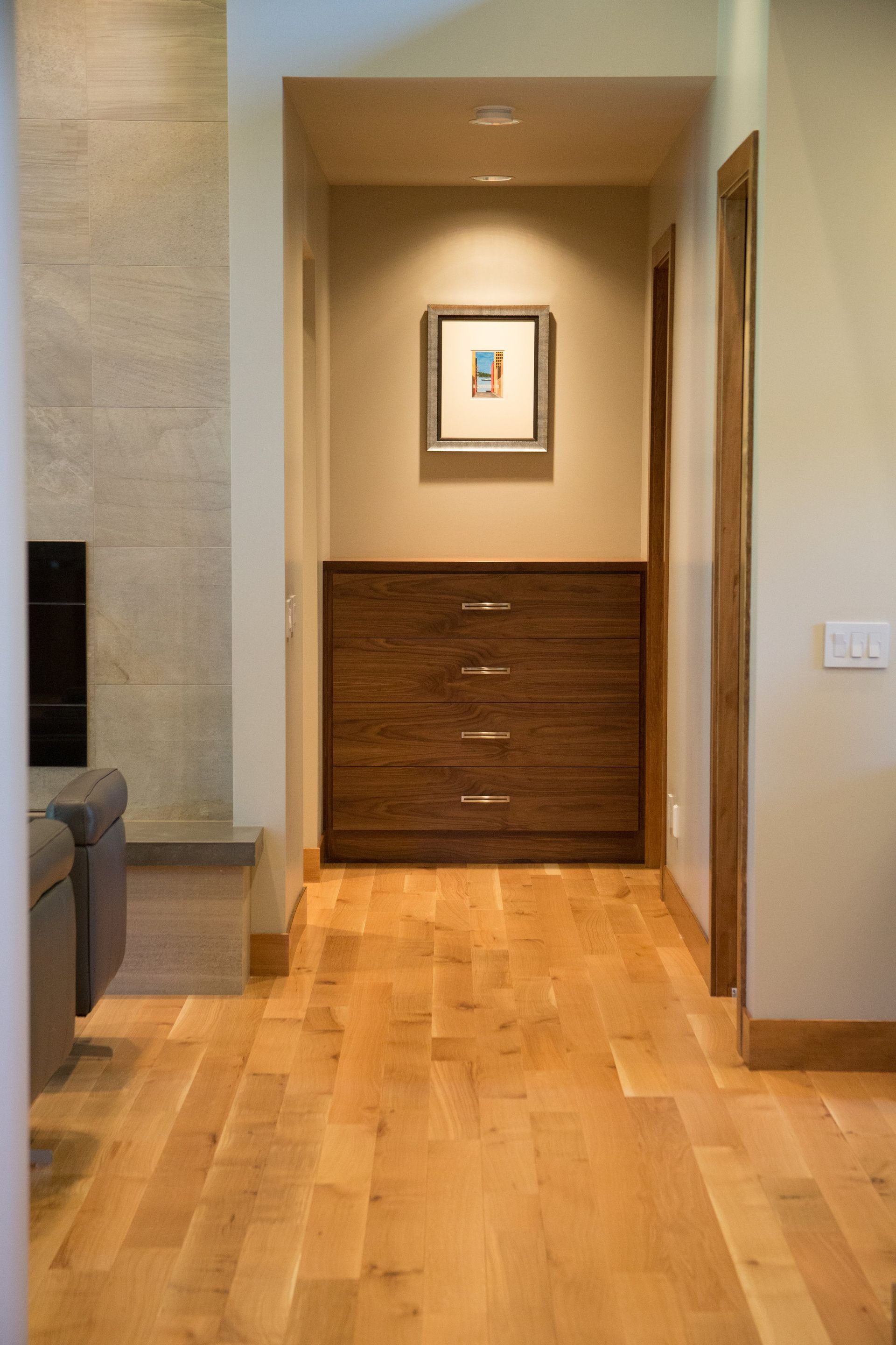 Hallway with light wood floors, beige walls, and a framed picture above a wooden cabinet.