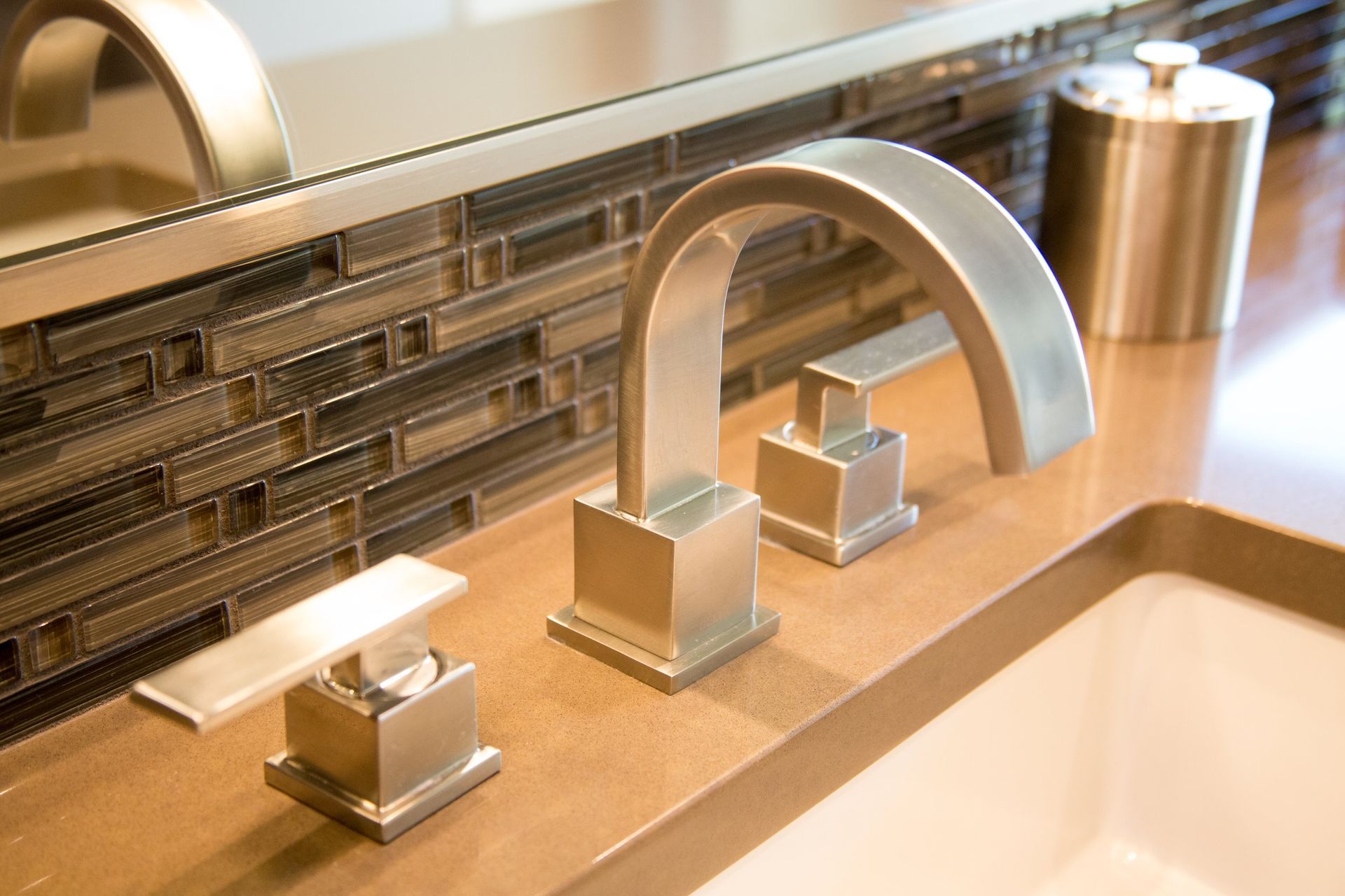 Modern bathroom sink with chrome faucet, soap dispenser, and mirrored mosaic tile backsplash