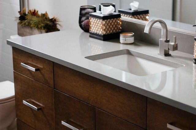 Bathroom vanity with dark wood cabinets, white countertop, and a sink with chrome faucet.