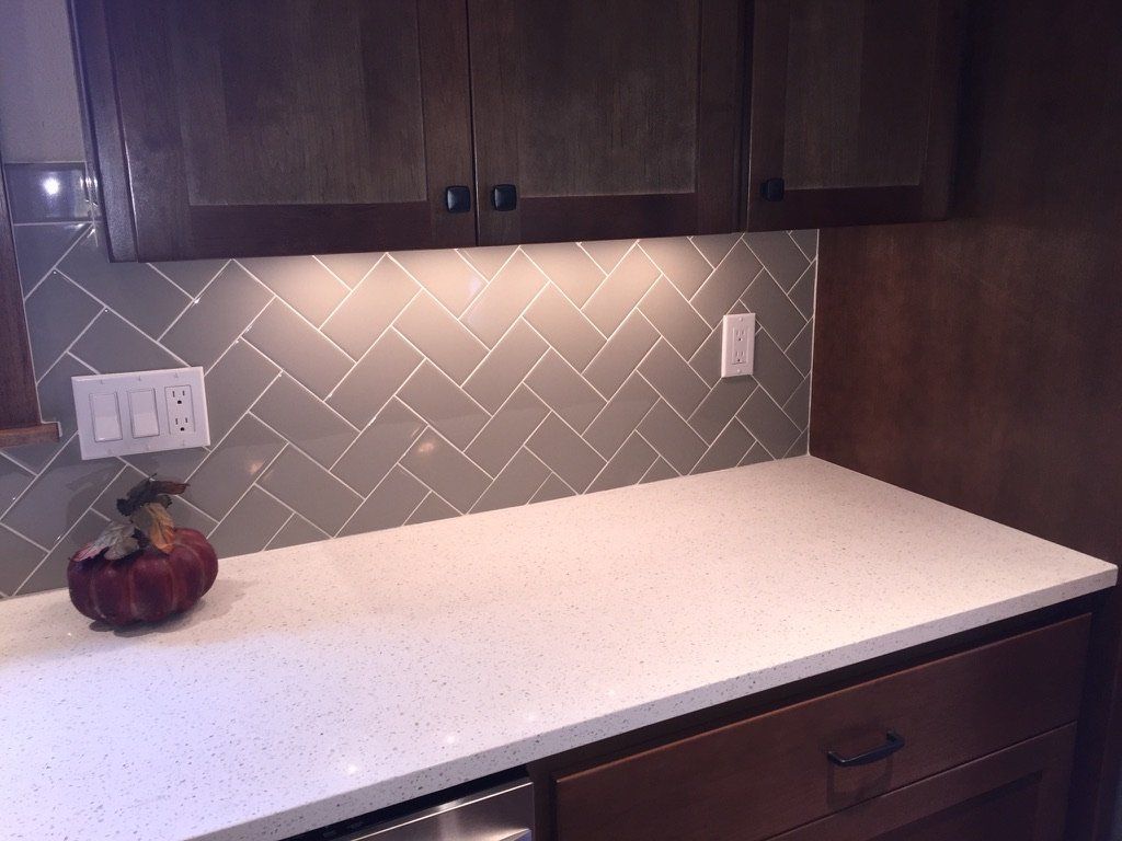 Kitchen countertop with dark cabinets, gray tile backsplash, and a bowl of fruit on the left.