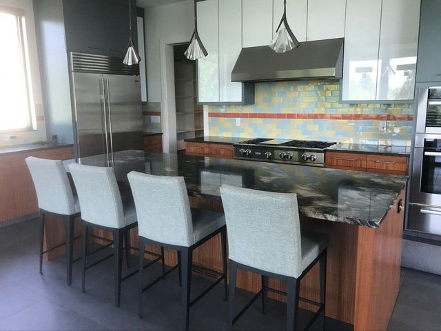Modern kitchen with island, four upholstered stools, stainless appliances, and colorful tile backsplash