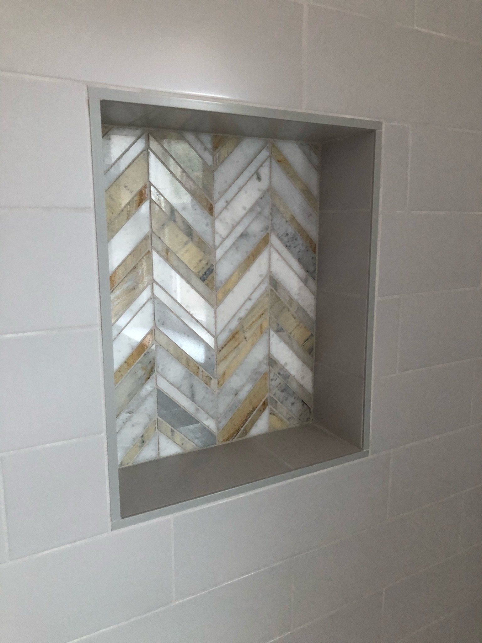 Tiled shower niche with a chevron-patterned mosaic back wall and gray tile surround