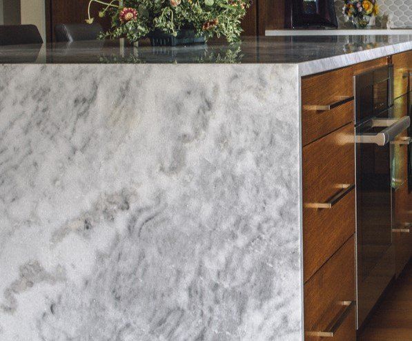 Modern kitchen counter with white marble front, wood cabinets, and granite countertop with flowers in the background