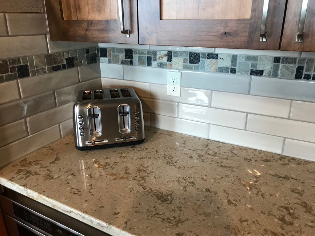 Kitchen countertop with stainless steel toaster, white tile backsplash, and wooden cabinets