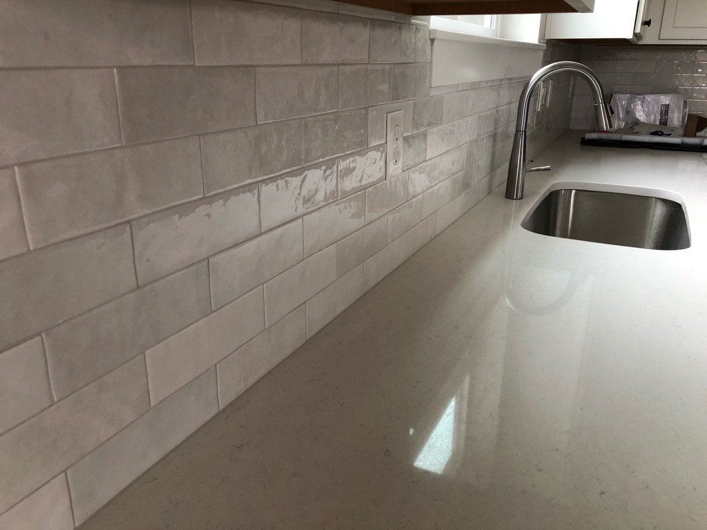 Modern kitchen countertop with light tile backsplash and stainless steel sink under a curved faucet