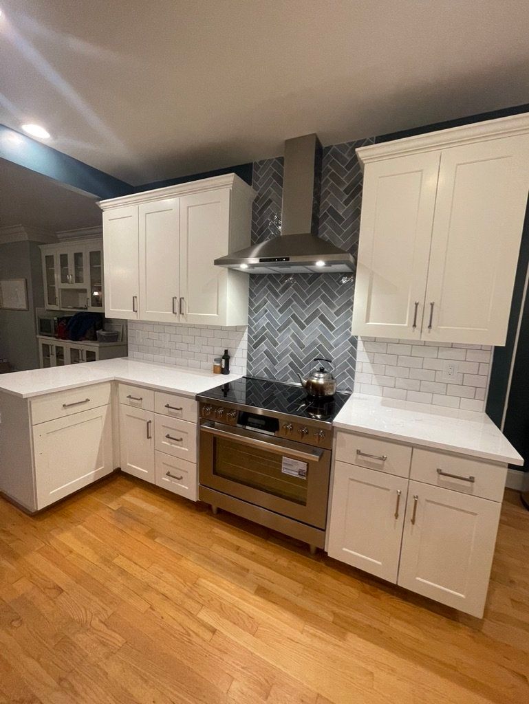 Modern white kitchen with herringbone tile backsplash, stainless steel range hood, and wood floors
