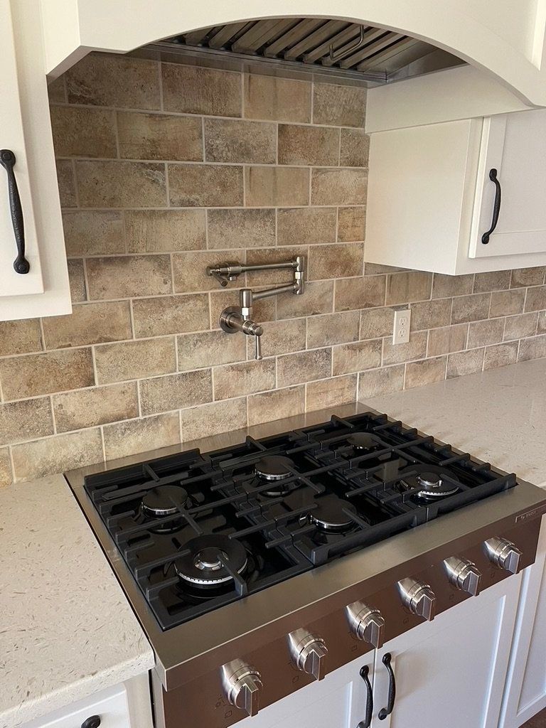 Modern kitchen with stainless gas range, beige tile backsplash, and arched vent hood