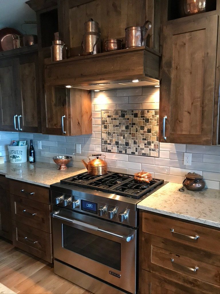 Rustic kitchen with wood cabinets, stainless stove, white tile backsplash, and warm under-cabinet lighting