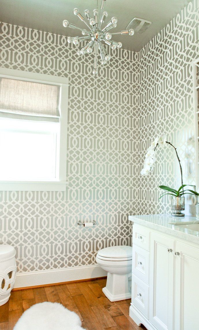 Elegant bathroom with patterned wallpaper, window, white vanity, toilet, and chandelier