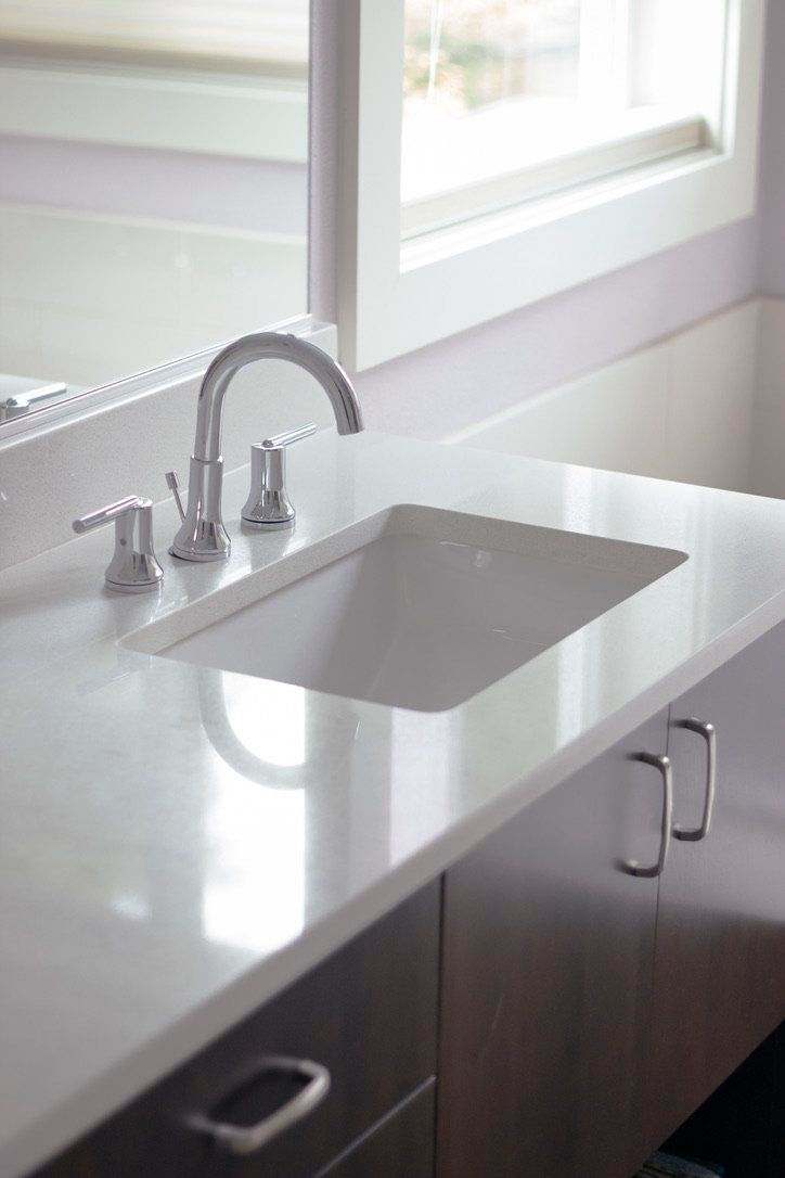 Modern kitchen sink with white countertop, chrome faucet, and dark wood cabinets by a window