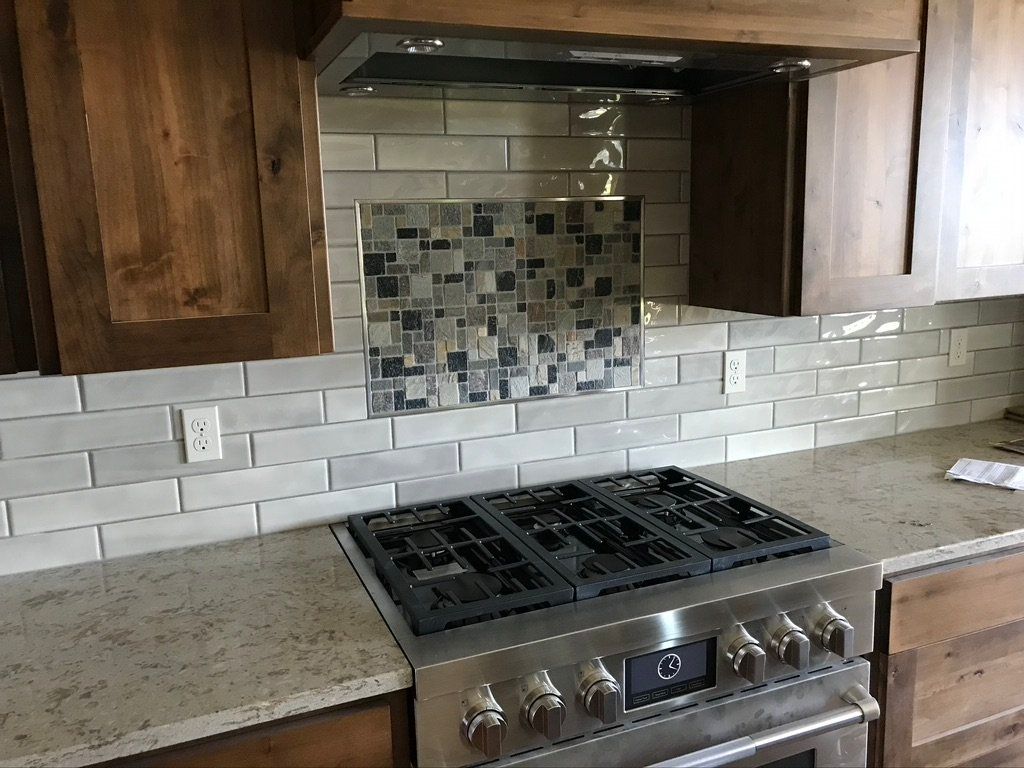 Modern kitchen with stainless steel gas range, granite countertops, white tile backsplash, and wood cabinets