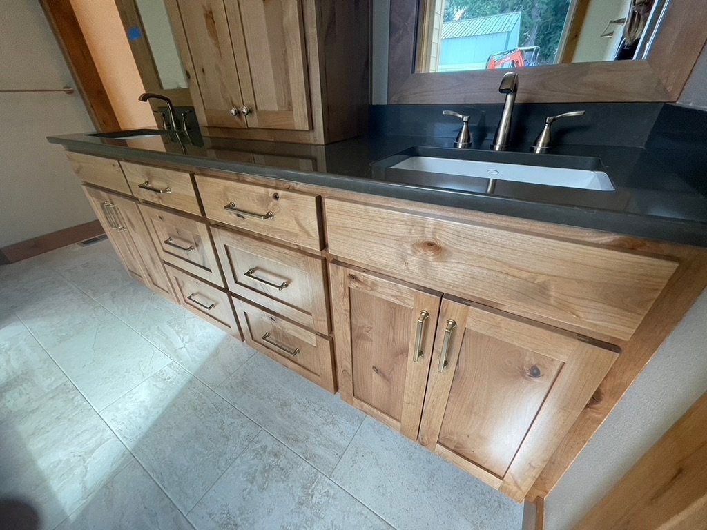 Wooden bathroom vanity with black countertop, sink, mirror, and cabinets in a tiled room