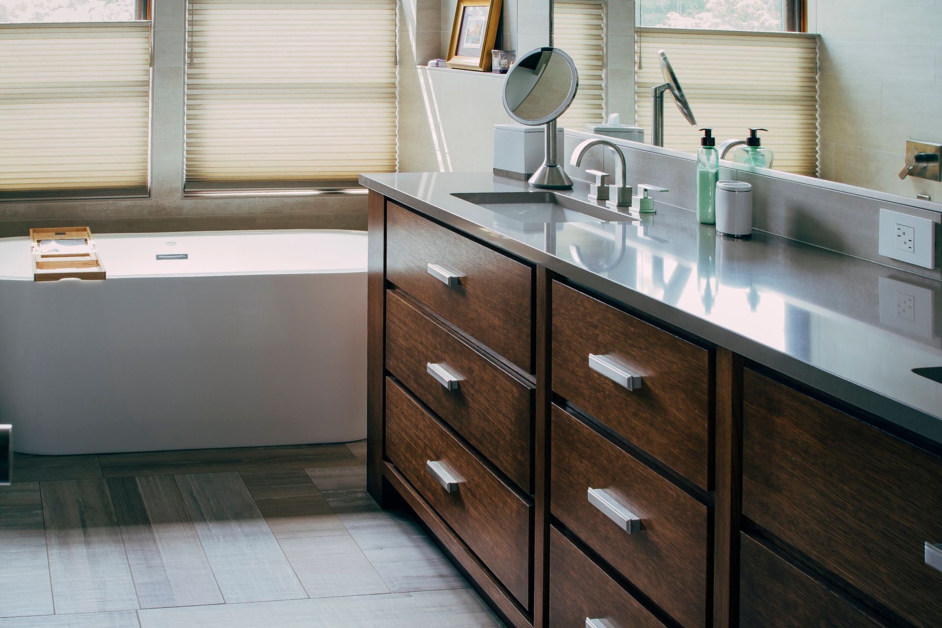 Modern bathroom vanity with wood cabinets, white countertop, mirror, and a sink by a window.