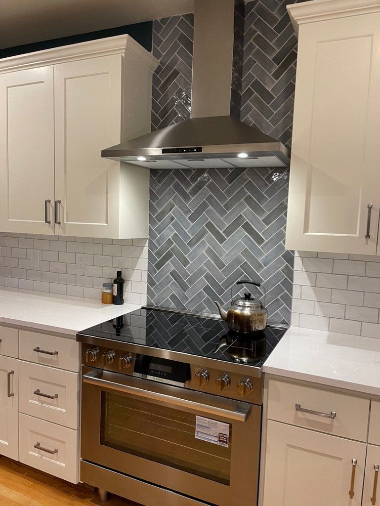 Modern kitchen with cream cabinets, stainless range hood, blue herringbone backsplash, and black countertop stove