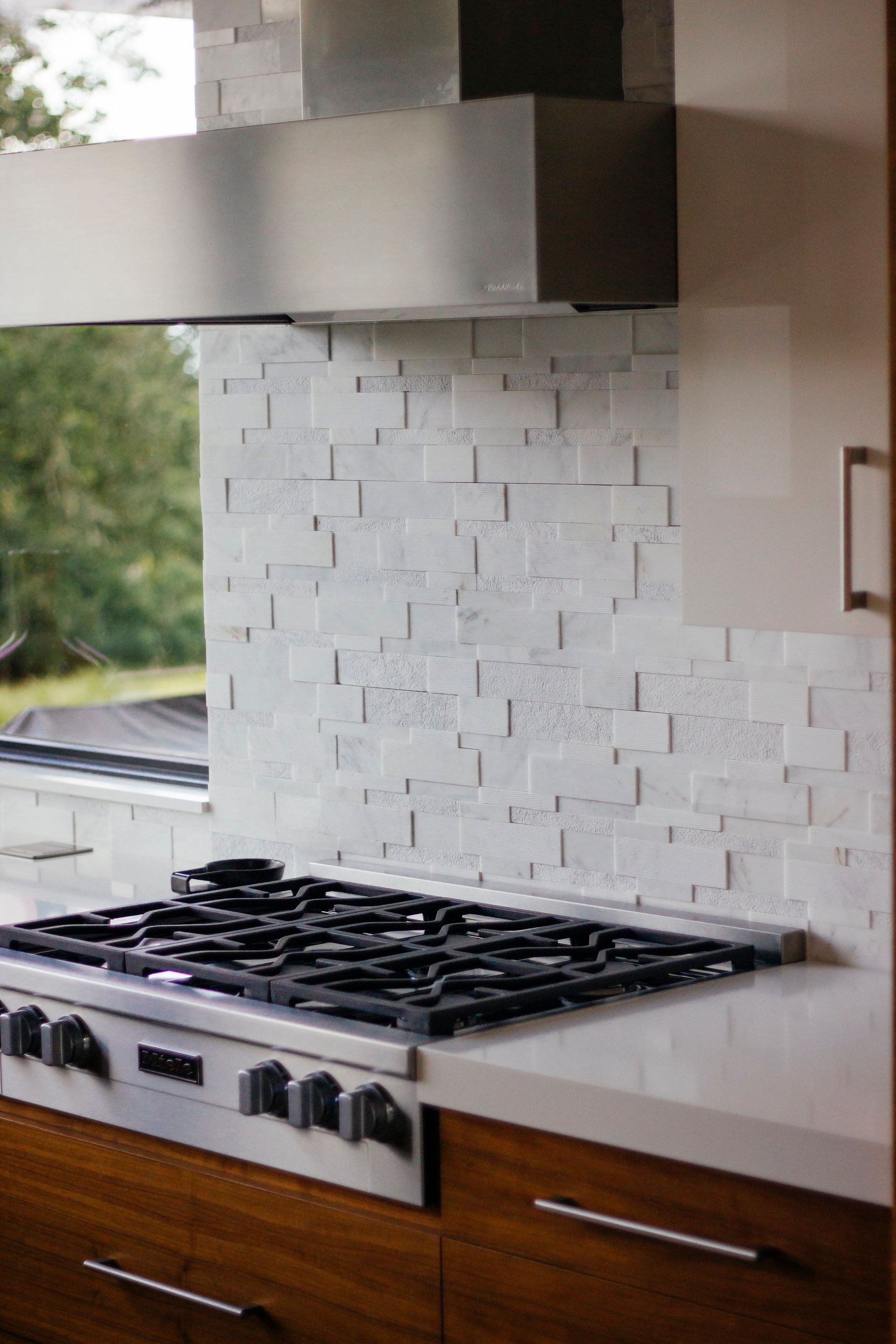 Modern kitchen stove with stainless hood, white tiled backsplash, and wood cabinets