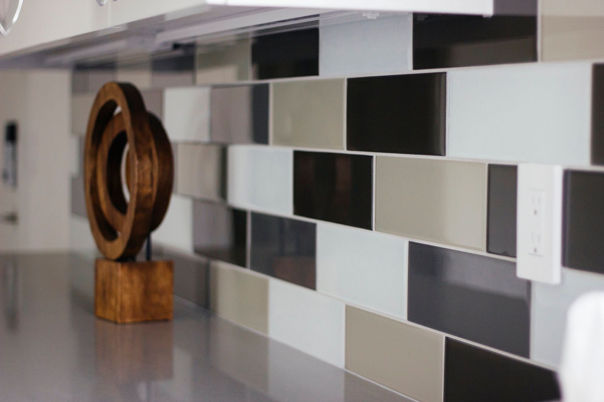 Modern kitchen backsplash with gray, white, and black tiles beside a wooden sculpture