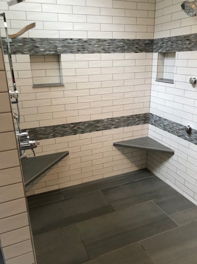 Accessible shower stall with gray tile, two wall benches, grab bar, and handheld showerhead.