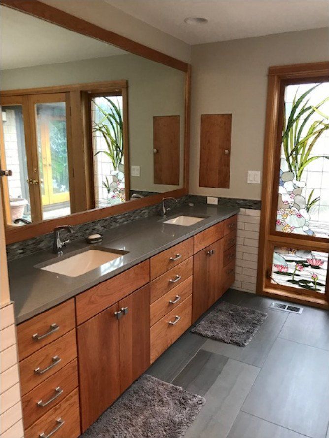 Modern bathroom vanity with double sinks, wood cabinets, large mirror, and windows overlooking greenery