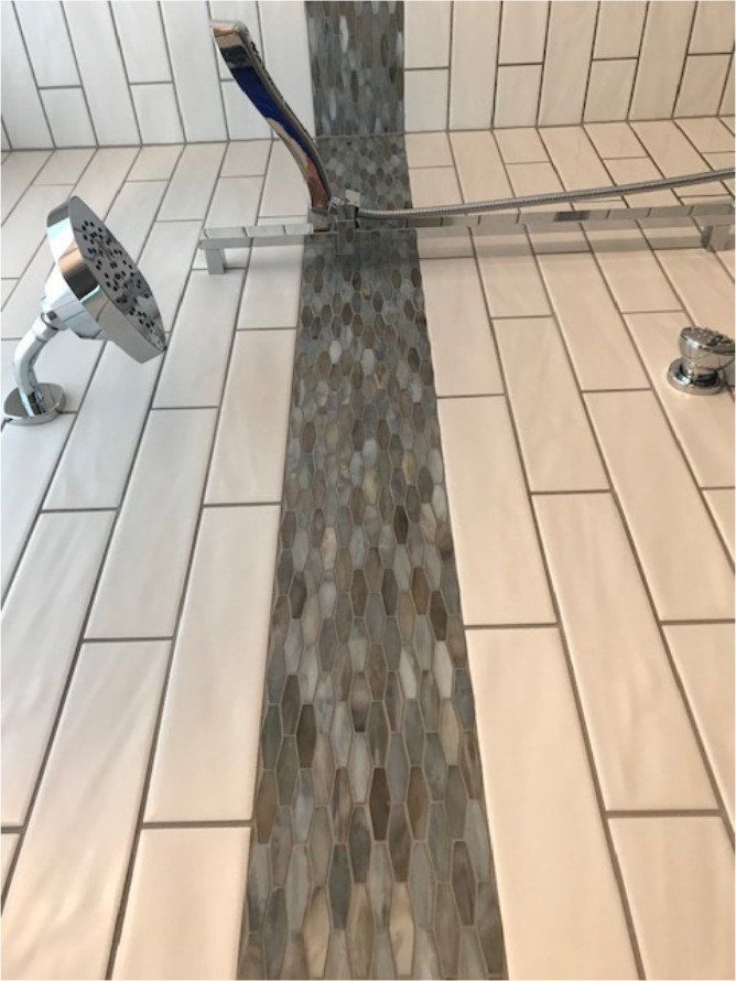 Bathroom floor with tiled walkway and two metal fixtures near a shower drain